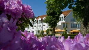 A hotel with white facades and red-tiled roofs, surrounded by lush greenery and purple flowers. - AKZENT Hotel Zur Post (Tabarz)