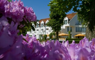 A hotel with white facades and red-tiled roofs, surrounded by lush greenery and purple flowers.