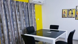 Una sala de reuniones con una mesa de vidrio, sillas negras, un panel blanco y una pared de acento amarilla.