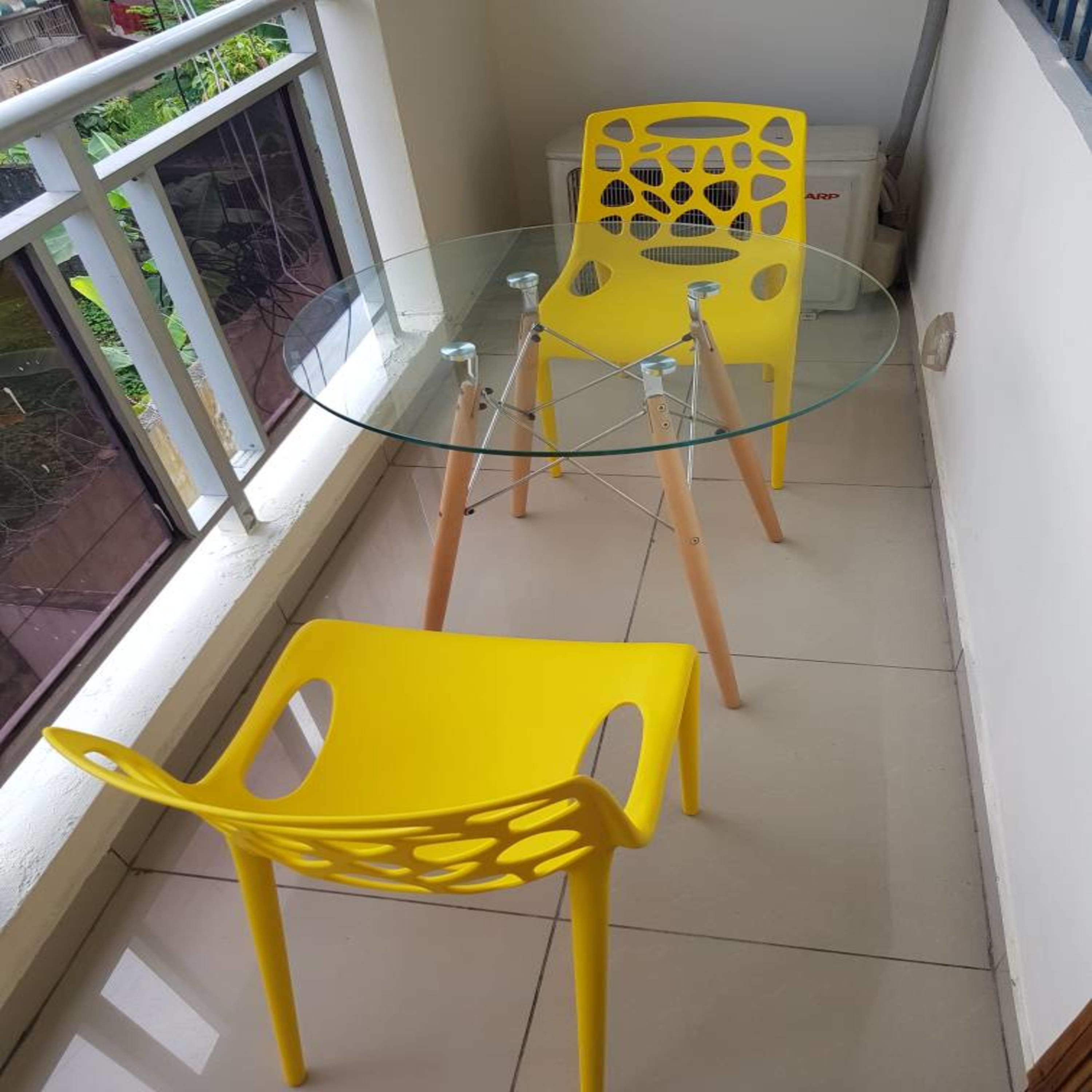 Uma varanda com mesa de vidro e duas cadeiras amarelas.