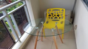 Un balcón con una mesa de vidrio y dos sillas amarillas.