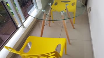 Uma varanda com mesa de vidro e duas cadeiras amarelas.