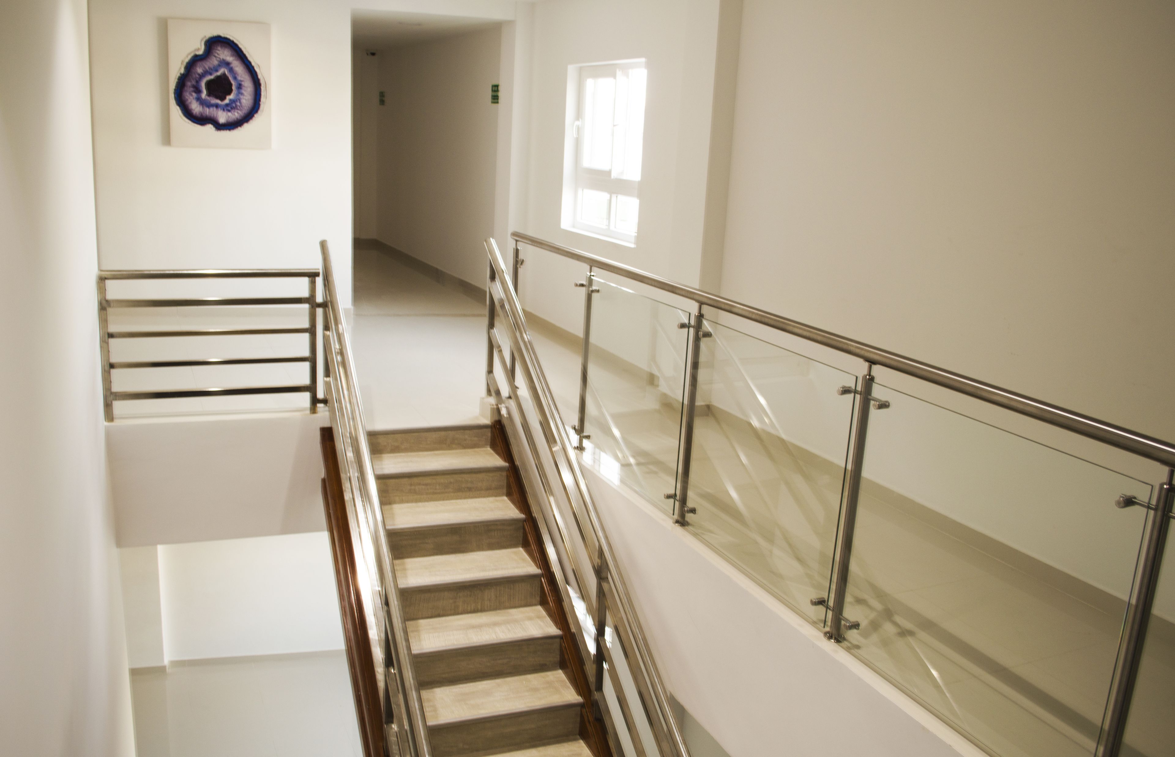 A staircase with metal railings and a glass balustrade, leading to a hallway with a door and a window.