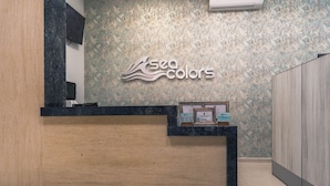 A reception desk with a 'sea colors' sign, a framed certificate, and a small display case. - Sea Colors Hotel (San Andrés)