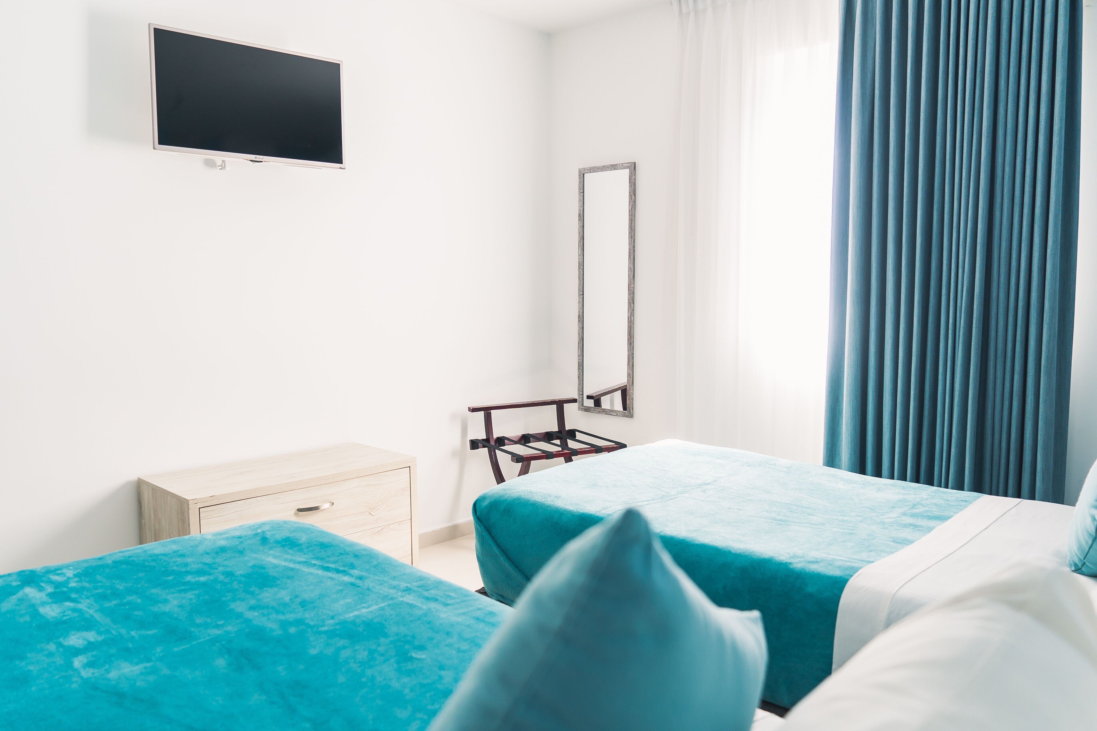 A hotel room with two beds, a TV, a mirror, and a window with curtains.