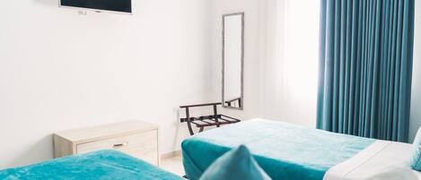 A hotel room with two beds, a TV, a mirror, and a window with curtains.