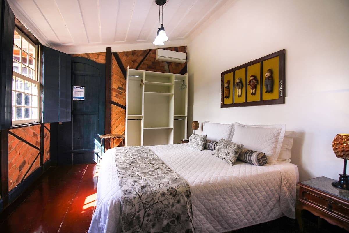 Quarto com cama, guarda-roupa, luminária pendente e um quadro na parede.