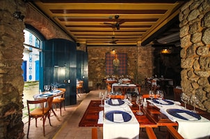 A restaurant with wooden tables and chairs, stone walls, and a view through an arched doorway.