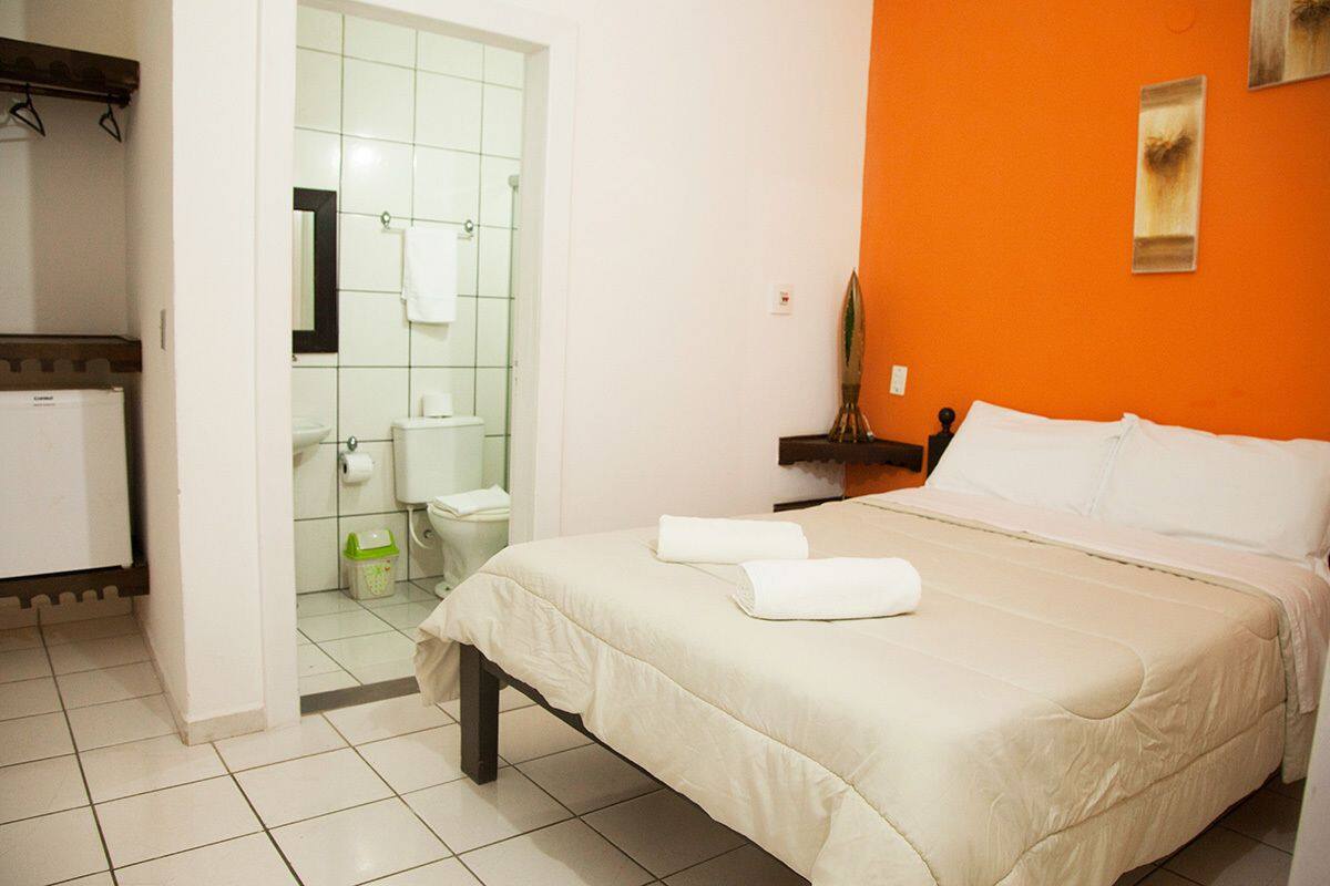 Une chambre d’hôtel avec un lit, une salle de bain et une petite étagère sur laquelle est posée une plante.