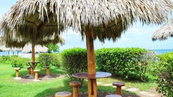 Estructura con techo de paja, una mesa y taburetes en un jardín.