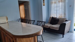 A dining area with a wooden table and chairs, a sofa, and a window with curtains. - Corinth Grove Apartment (St. David)