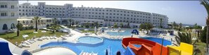 A hotel with multiple swimming pools, a water slide, and a large building in the background. - Palmyra Holiday Resort & Spa (Monastir)