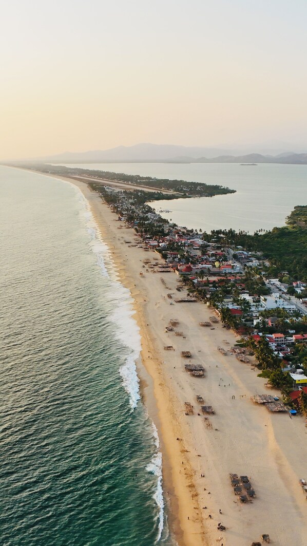 Vista aérea de un pueblo costero con una extensa playa, viviendas densas y una clara visión del mar.