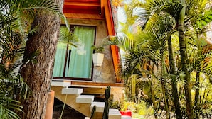 A tree-lined pathway leading to a wooden building with a staircase and a window with a green curtain. - A&V Hotel Boutique (Coyuca de Benitez)