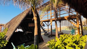 A beachside structure with a thatched roof, surrounded by lush greenery and a clear view of the ocean. - A&V Hotel Boutique (Coyuca de Benitez)