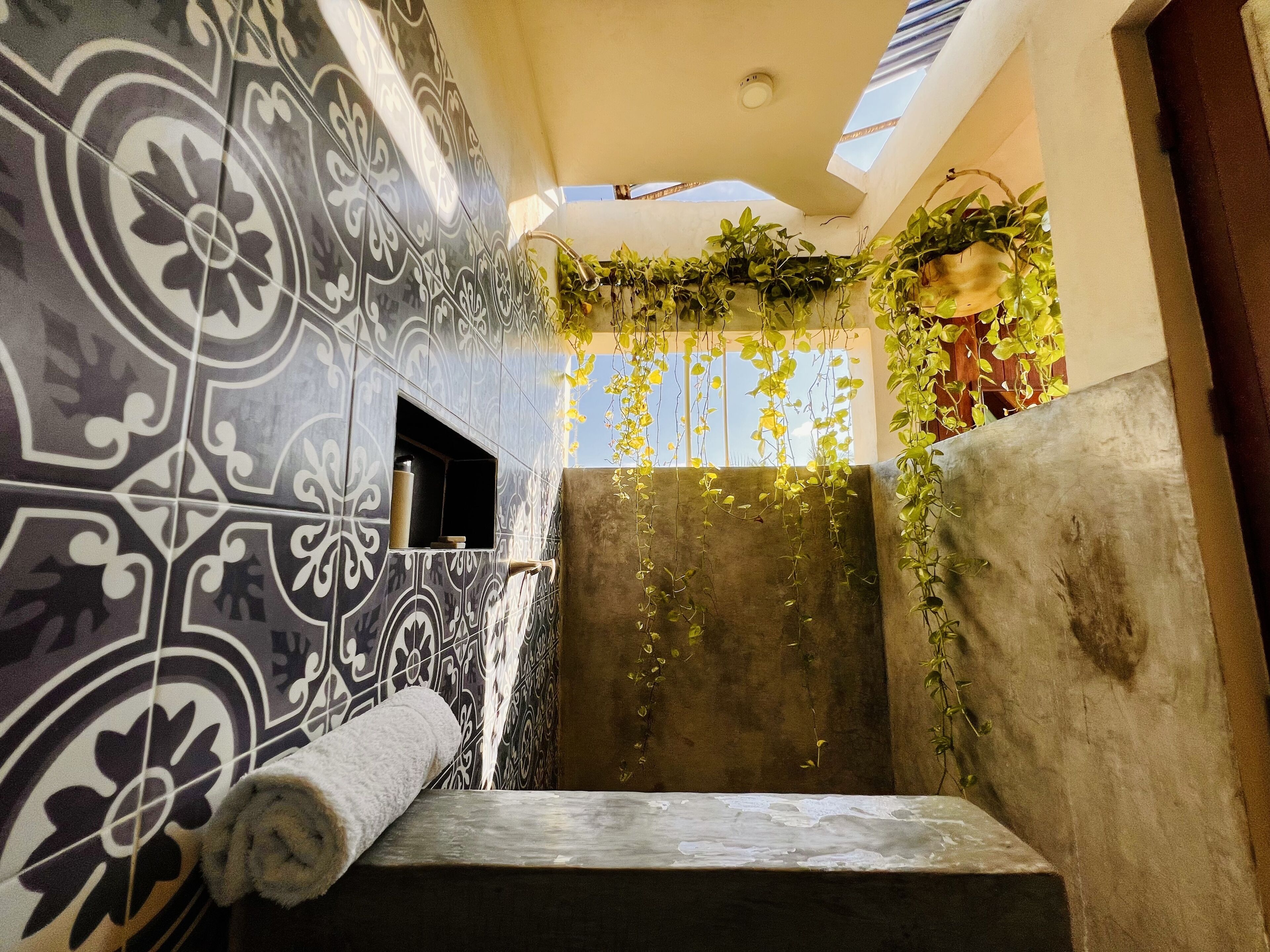 A bathroom with patterned tiles, a towel, a shower area, and hanging plants.