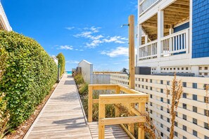 A wooden pathway leading to a building with a balcony overlooking a beach.