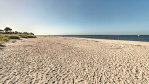 Une vaste plage de sable où l’on peut voir des traces de pneus menant à l’eau, un ciel dégagé et quelques personnes au loin.