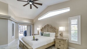 Une chambre à coucher avec un grand lit, une table de chevet, un ventilateur de plafond et une fenêtre avec des stores.