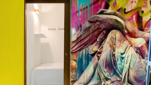 A hotel room with a bed, a colorful mural, and a door with a sign that reads "Dear bed." - Hostel Tropico 20º OceanFront (Cozumel)