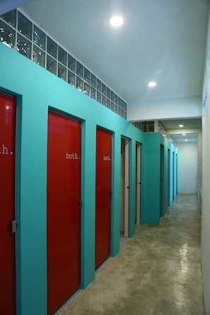 Un couloir avec des portes rouges portant l’inscription « pour les deux sexes » et des murs de couleur turquoise.