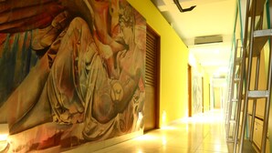 A hallway with a large mural of a reclining figure, a tiled floor, and a staircase with metal railings. - Hostel Tropico 20º OceanFront (Cozumel)