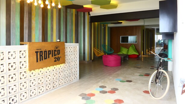 A modern hotel lobby with a colorful hexagonal floor pattern, a bike parked by the wall, and a sign indicating 'TRÓPICO 20°'. - Hostel Tropico 20º OceanFront (Cozumel)