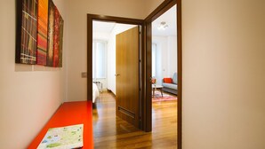 Un pasillo con piso de madera, un banco rojo y una puerta que da a una sala de estar con sofá y alfombra.