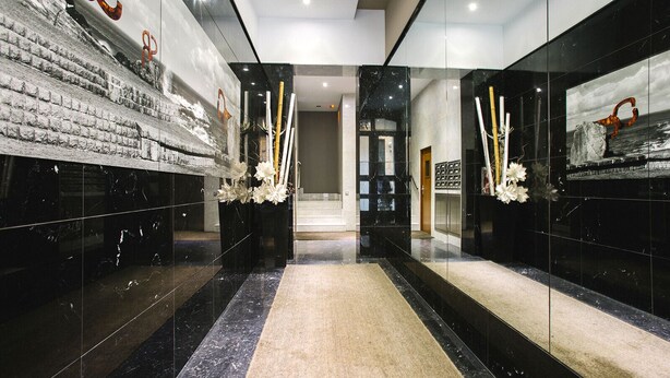 Un moderno vestíbulo de hotel con pisos de mármol, paredes de vidrio y una escalera central.