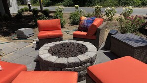 Ein Patio mit Sitzgelegenheiten im Freien, einem Steinkamin und umliegendem Grün.