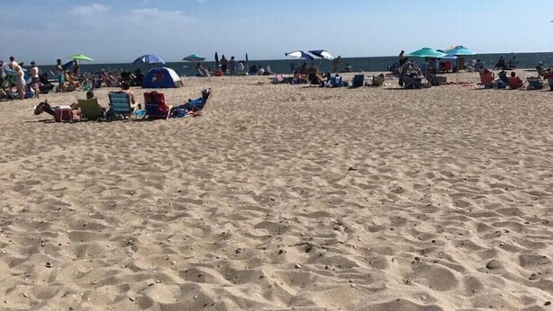 Ein Sandstrand mit Menschen, Zelten und Sonnenschirmen.