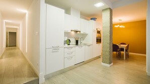 Een moderne keuken met witte kasten, een inbouwoven en een eethoek met een tafel en stoelen.
