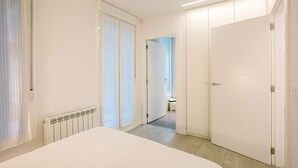 Een hotelkamer met een groot bed, een radiator, een deur en een gang naar een andere kamer.