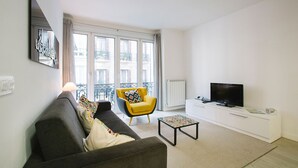 Een moderne woonkamer met een grijze bank, een geel fauteuil, een salontafel, een televisie en een witte kast.