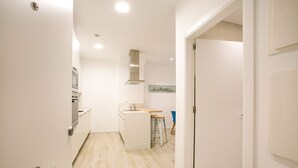Una cocina moderna con armarios blancos, una campana extractora de acero inoxidable y una pequeña isla con taburetes.