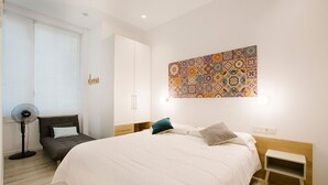 Un dormitorio moderno con una cama grande, un ventilador de pie, un armario y una llamativa obra de arte en la pared.