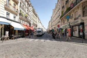 Una calle adoquinada flanqueada por edificios de varios pisos, algunos con balcones y escaparates.