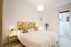 A bedroom with two beds, a ceiling fan, a nightstand with a lamp, and a cactus-patterned headboard.