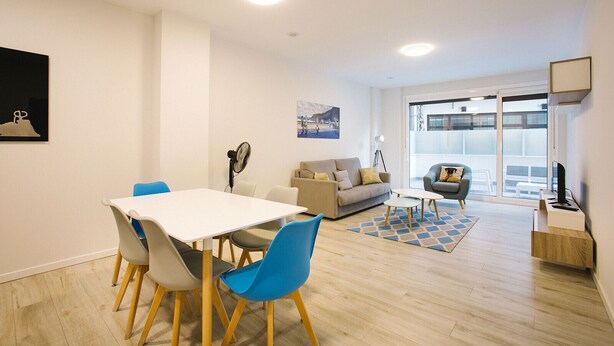 Un salon moderne comprenant un coin repas, un canapé, un fauteuil et une grande fenêtre.