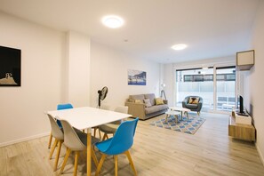 A modern living room with a dining area, a sofa, a chair, and a large window. - Gloria Suites 3 - 2 dormitorios (San Sebastián)