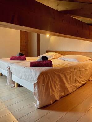 A room with two beds, wooden flooring, and a sloped ceiling.