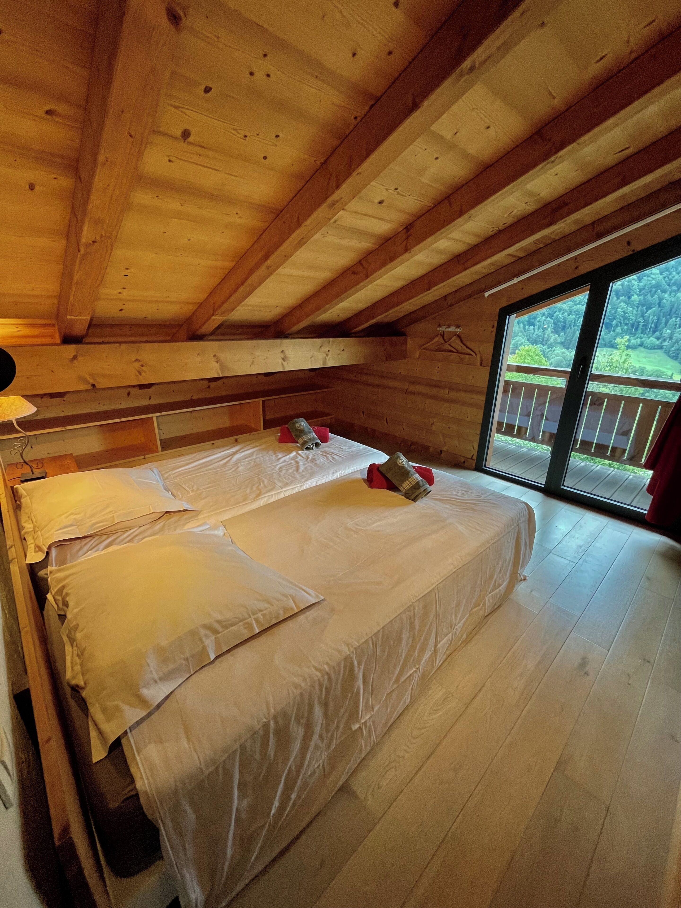 A wooden cabin bedroom with a large bed, a window, and a view of a forest.