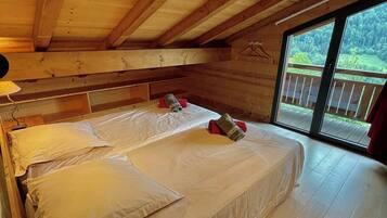 A wooden cabin bedroom with a large bed, a window, and a view of a forest.