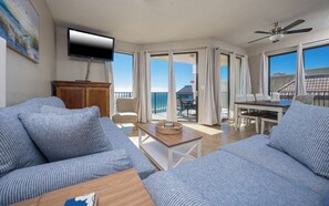 Een ruime woonkamer met een grote bank, een televisie en een balkon met een eethoek.