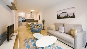 A modern living room with a sofa, armchair, and coffee table. A kitchen is visible in the background with a dining area. - M Gloria Suites 5 1C  inner courtyard, one bedroom (San Sebastián)