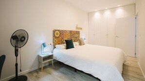 A bedroom with a bed, a bedside table, a lamp, a standing fan, and a wardrobe. - M Gloria Suites 5 1C  inner courtyard, one bedroom (San Sebastián)