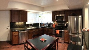 A modern kitchen with dark wood cabinets, stainless steel appliances, and a black granite countertop.