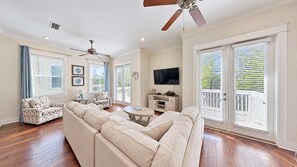 A spacious living room with a large sectional sofa, a coffee table, a television, and a ceiling fan.