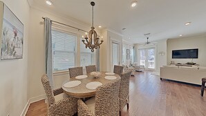 A spacious dining area with a round table and woven chairs, a chandelier, and a large window with blinds. - "Mint Julep" at Prominence - 3 BR/ 2.5 BA - Sleeps 9 - Six Passenger LSV Included! (Watersound)