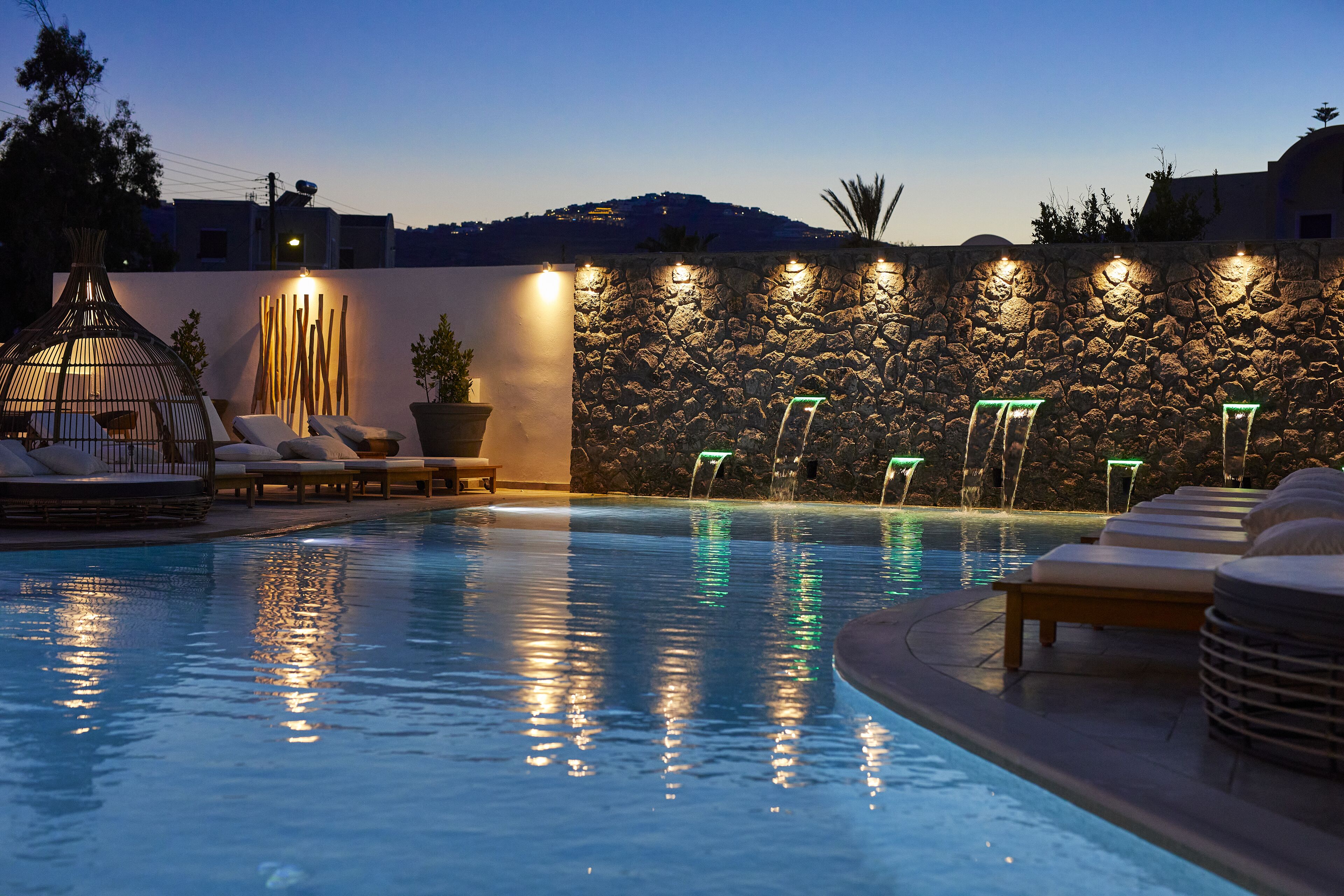 Una piscina con sillones de descanso y un muro de piedra con luces.